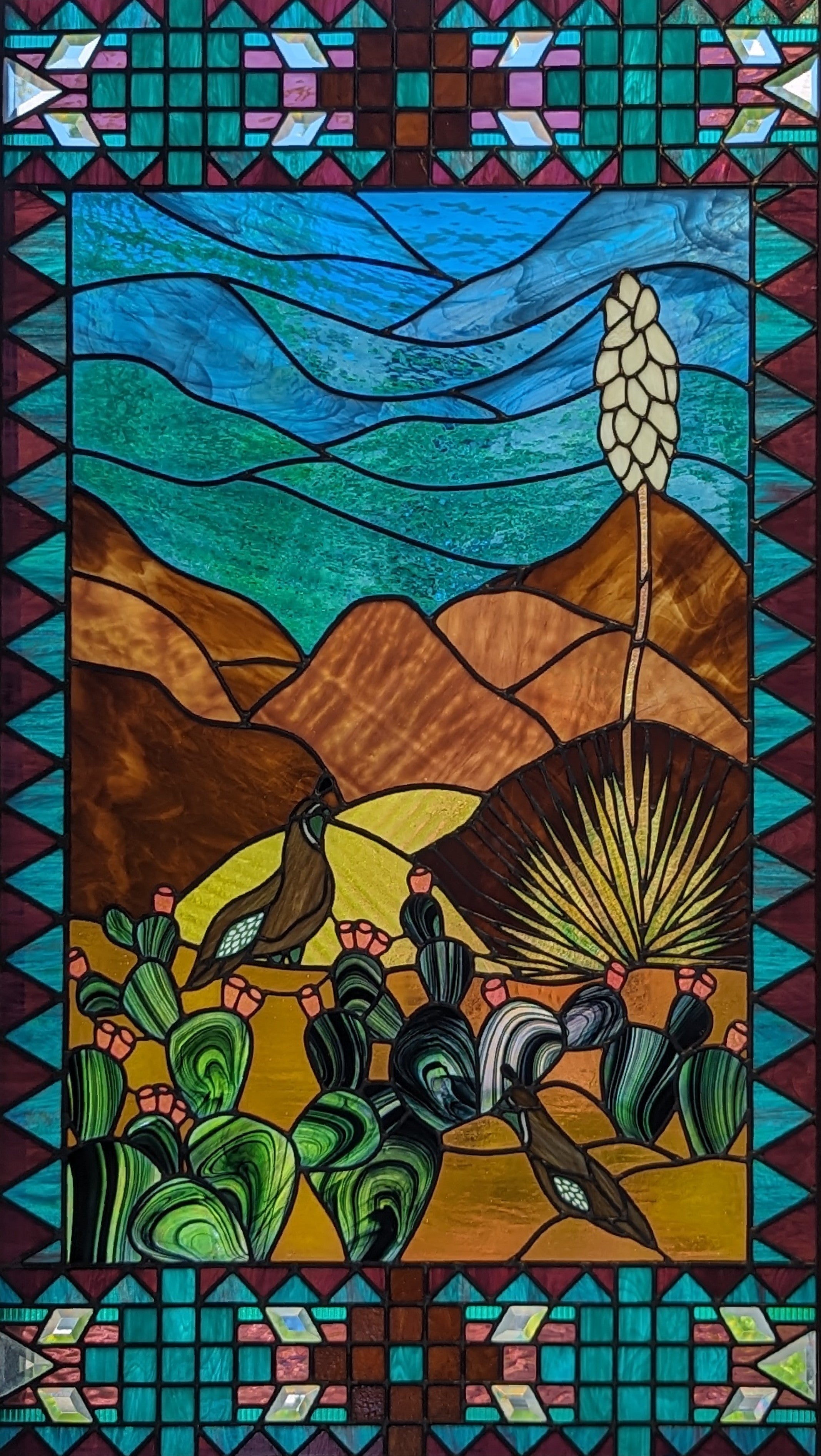 new mexican original stained glass with vibrant teals, blues, and desert cyans featuring the rolling hills, desert plants, and two quails. cactus and blooms also ordain the scene